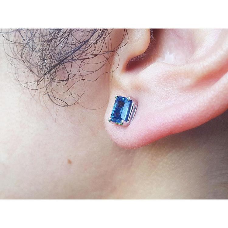 Blue sapphire gemstone earring worn on an ear with a plain background