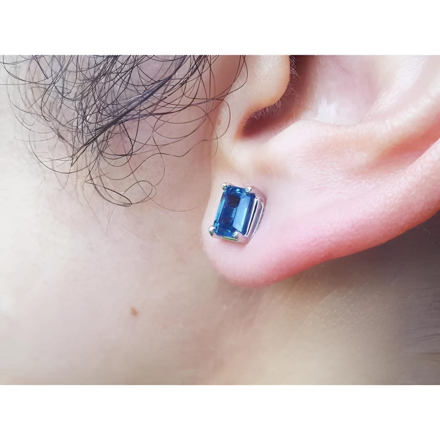 Emerald cut deep blue sapphire stud earring in 14K white gold worn on an ear.
