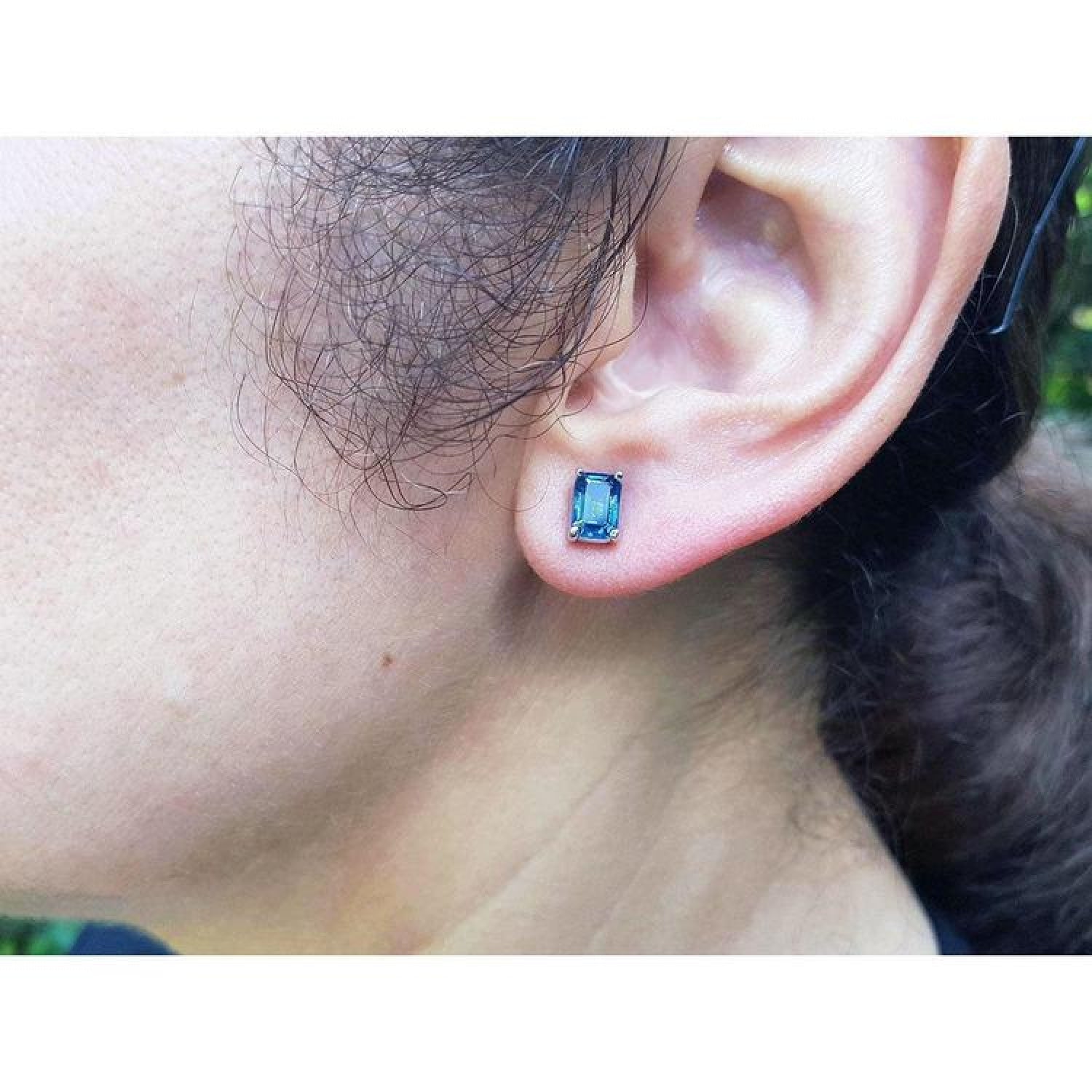 Emerald cut deep blue sapphire solitaire stud earring in 14K white gold on an ear.