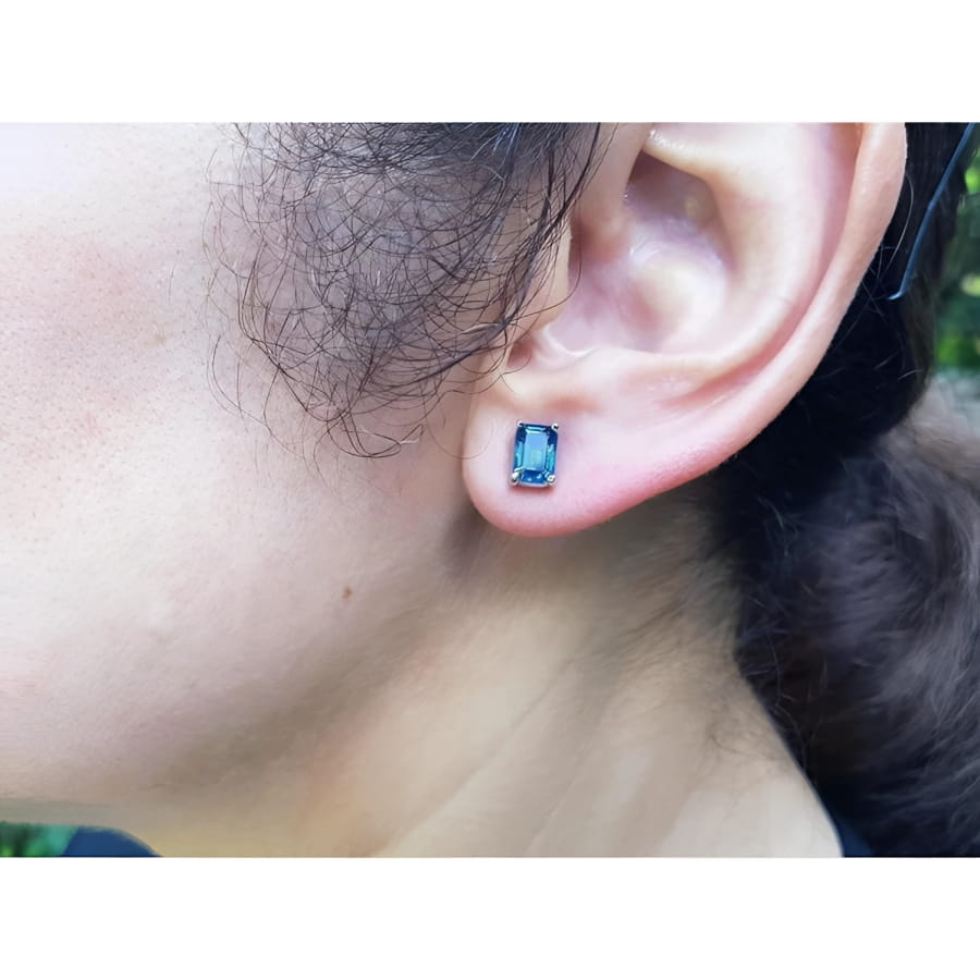Emerald cut deep blue sapphire solitaire stud earring in 14K white gold on an ear.