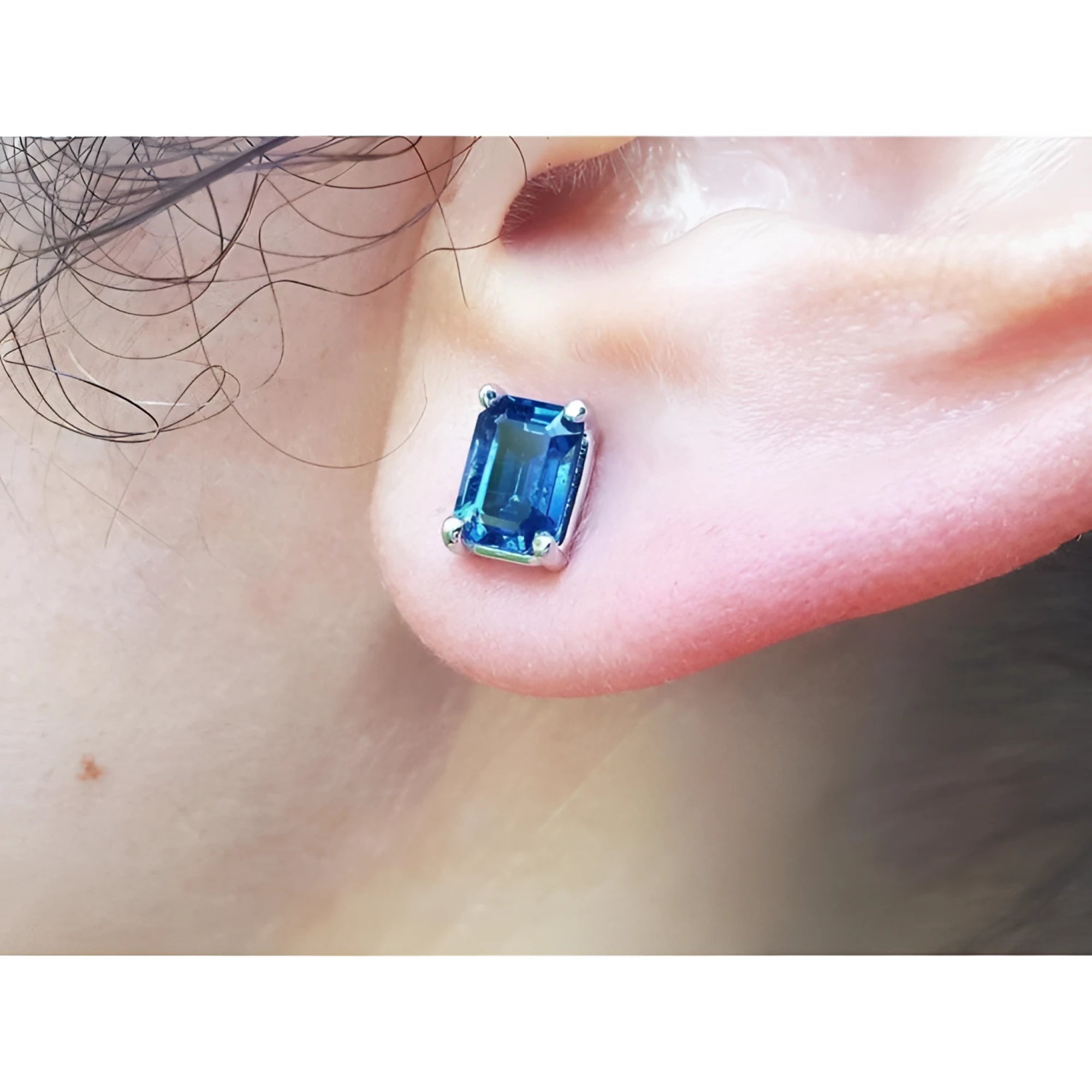 Blue natural sapphire earring set in 14k white gold on a person's ear.