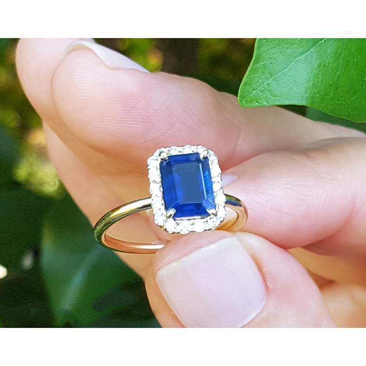 Gold ring 14k with a blue natural sapphire held between fingers against a green leafy background