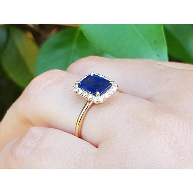 14k yellow gold ring with a blue natural sapphire on a finger against a green leafy background