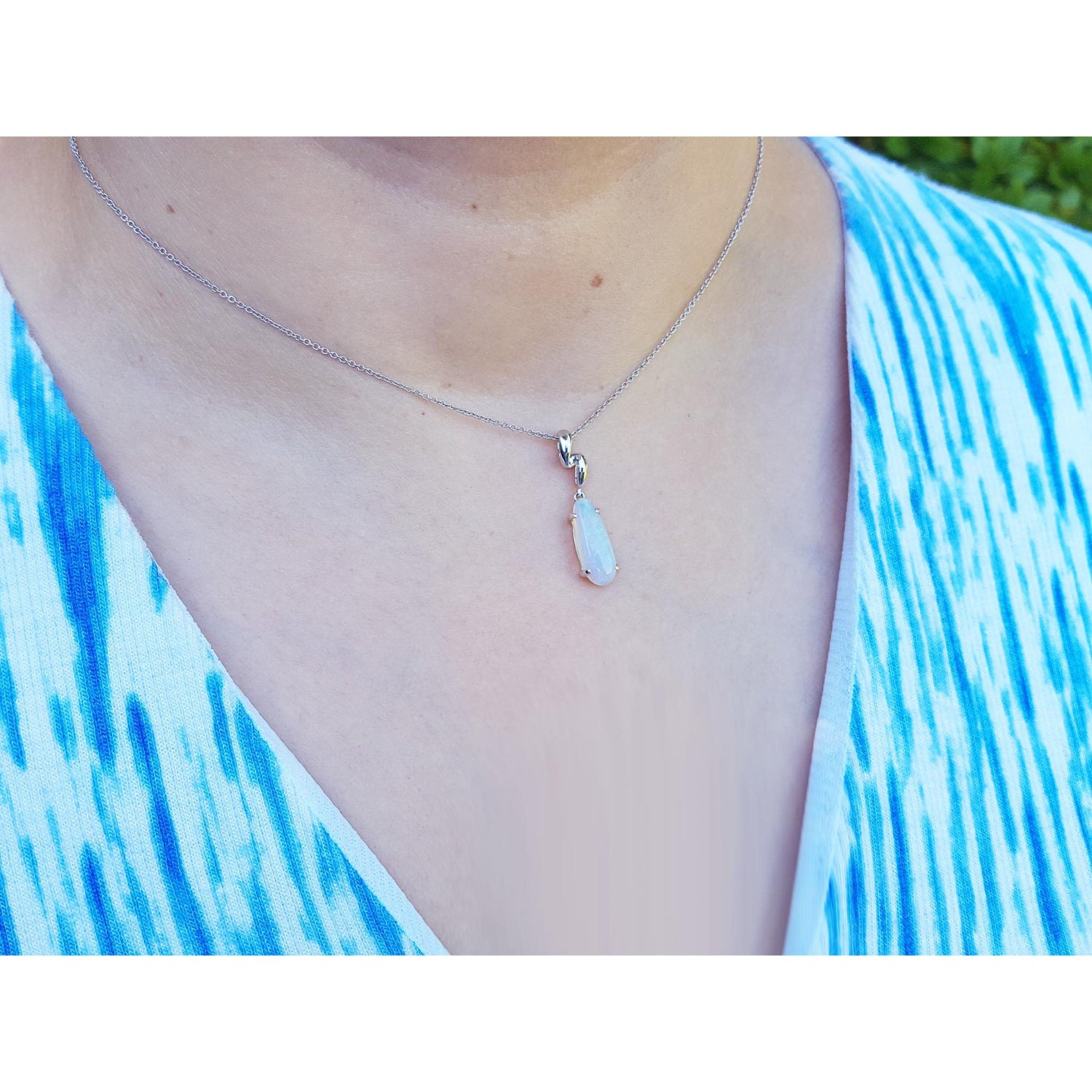 Necklace with a teardrop-shaped opal pendant worn by a person in a blue and white patterned top.