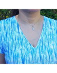 Person wearing an opal pendant in a blue and white tie-dye shirt with a blurred green background.
