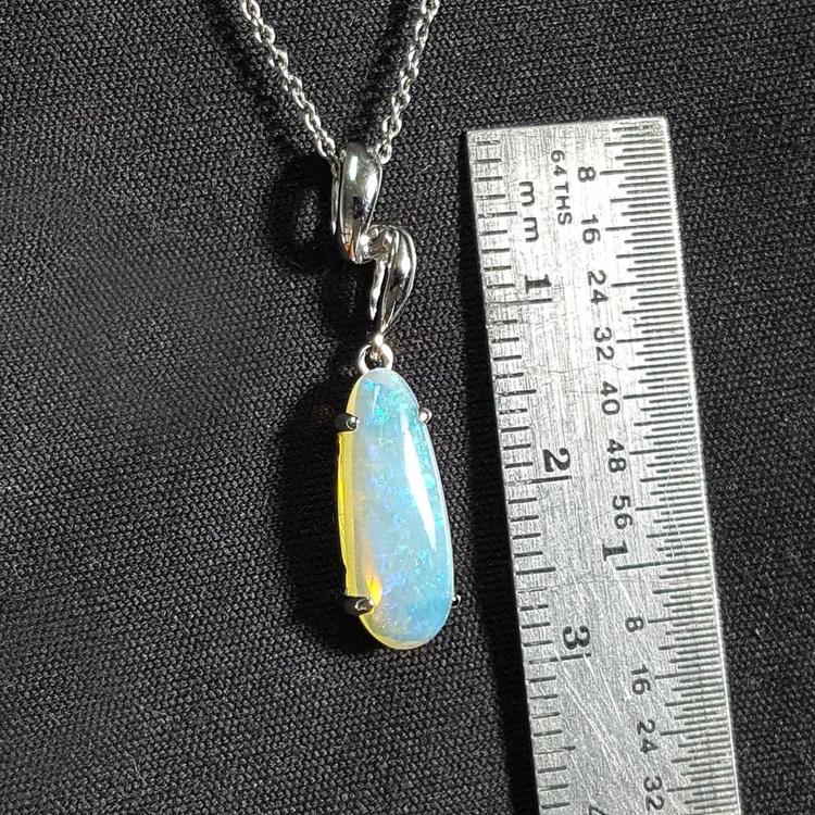 Opal pendant on a chain with a ruler for scale against a black background