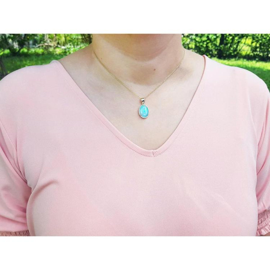 Natural Australian opal pendant with bluish green oval opal in 14K yellow gold, worn on a peach top.