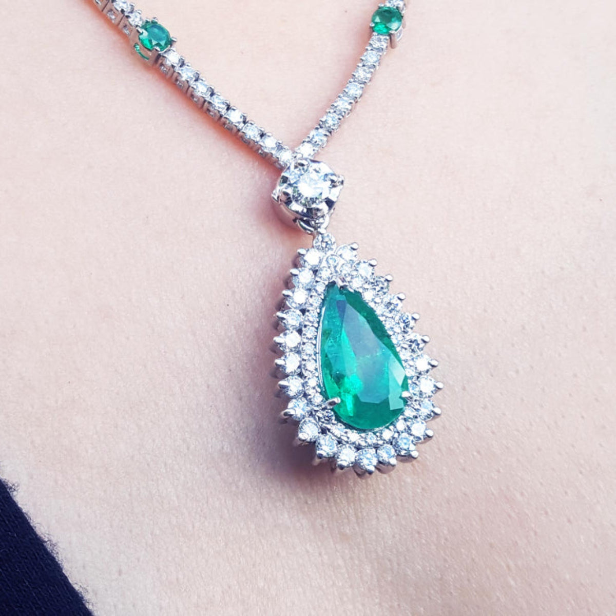 Green teardrop emerald pendant with double halo of diamond accents on a Leidy&#39;s neck