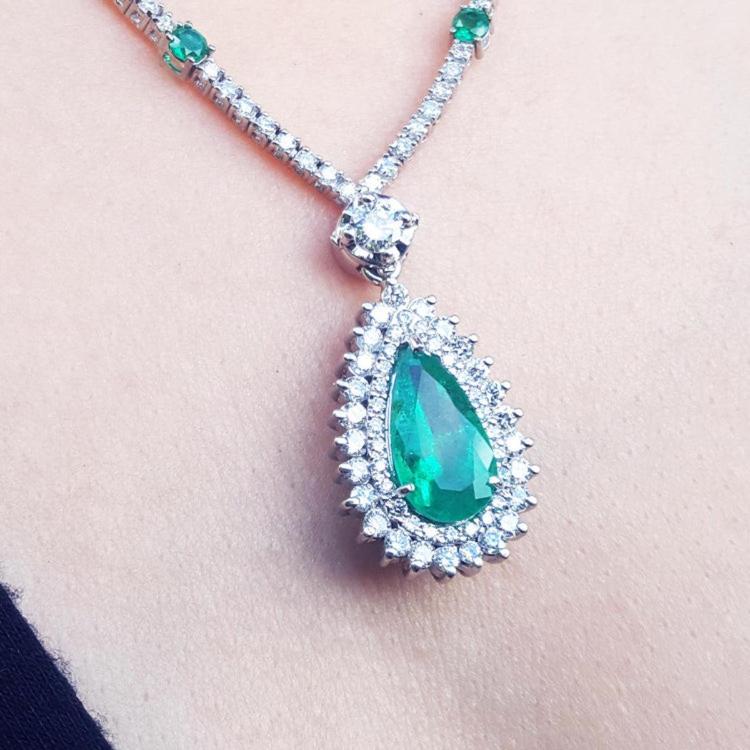 Green teardrop emerald pendant with double halo of diamond accents on a Leidy's neck