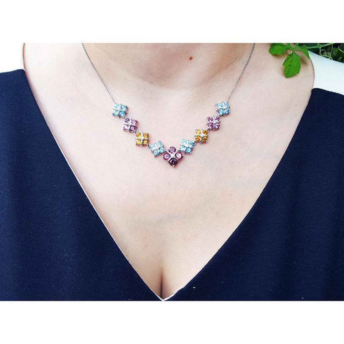 18K white gold necklace with tri-colored topaz X-cluster links on a woman's neck.
