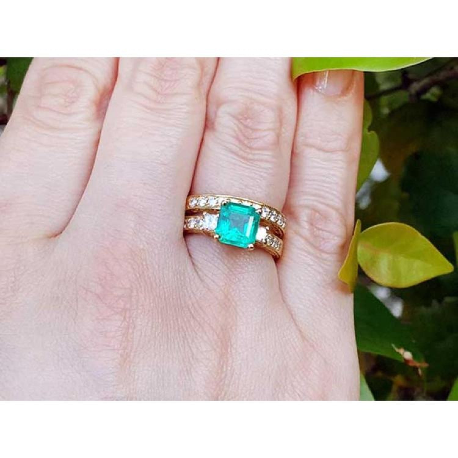 14K gold bridal emerald ring with matching diamond wedding band on a finger.