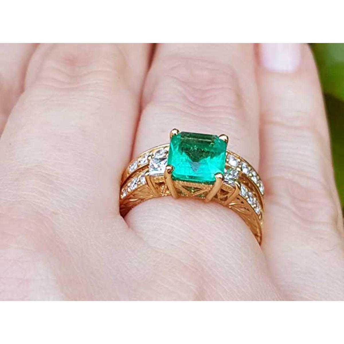 Gold ring with a square emerald on a finger.