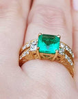 Gold ring with a square emerald on a finger.