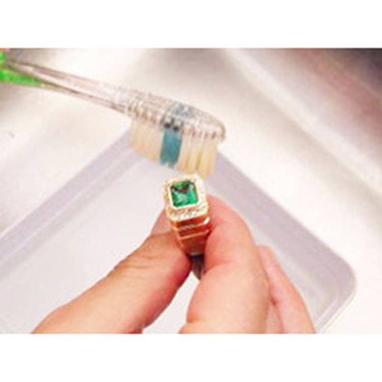 Brushing emerald ring on top side main gemstone and accent diamonds removing dirt