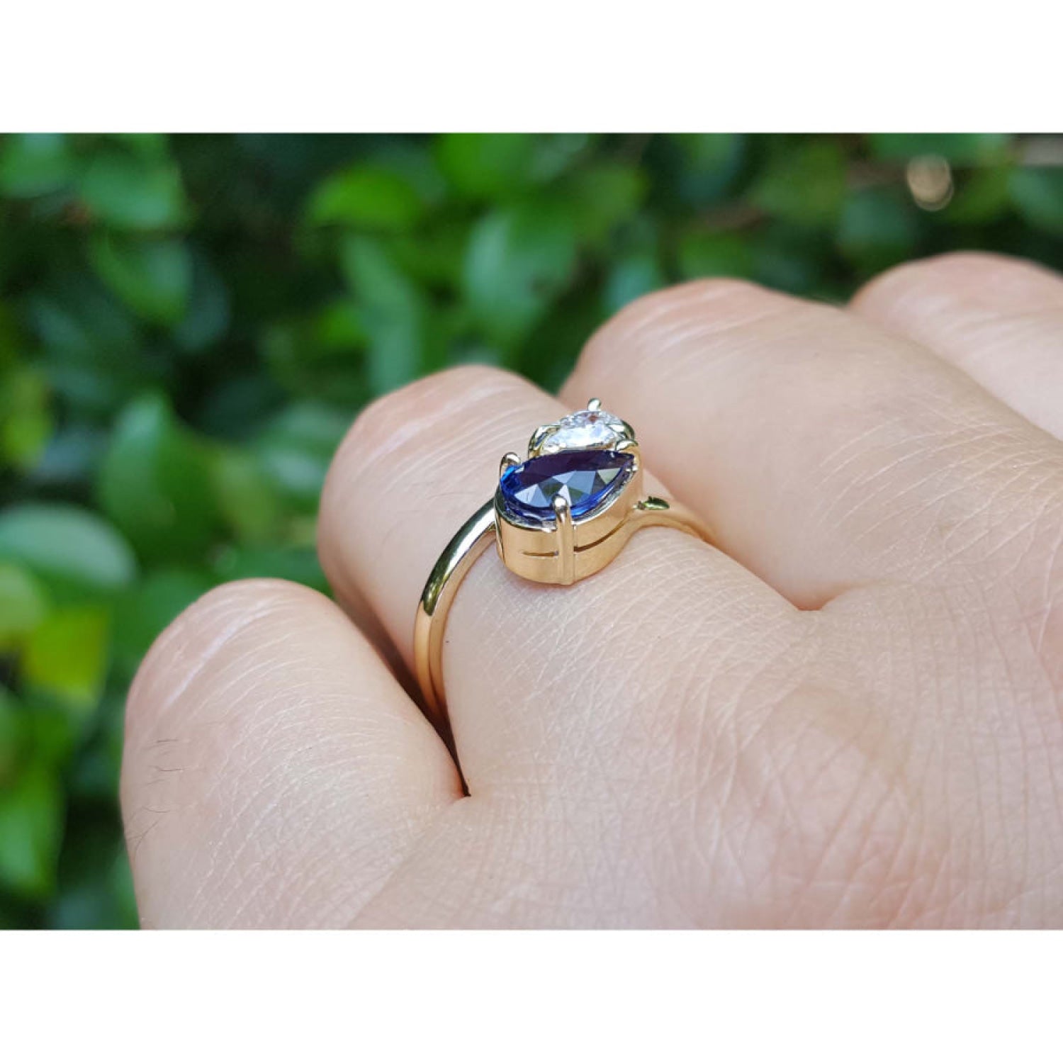 On a finger a Two-stone "You and Me" blue natural sapphire bypass ring handcrafted in 18k yellow gold.