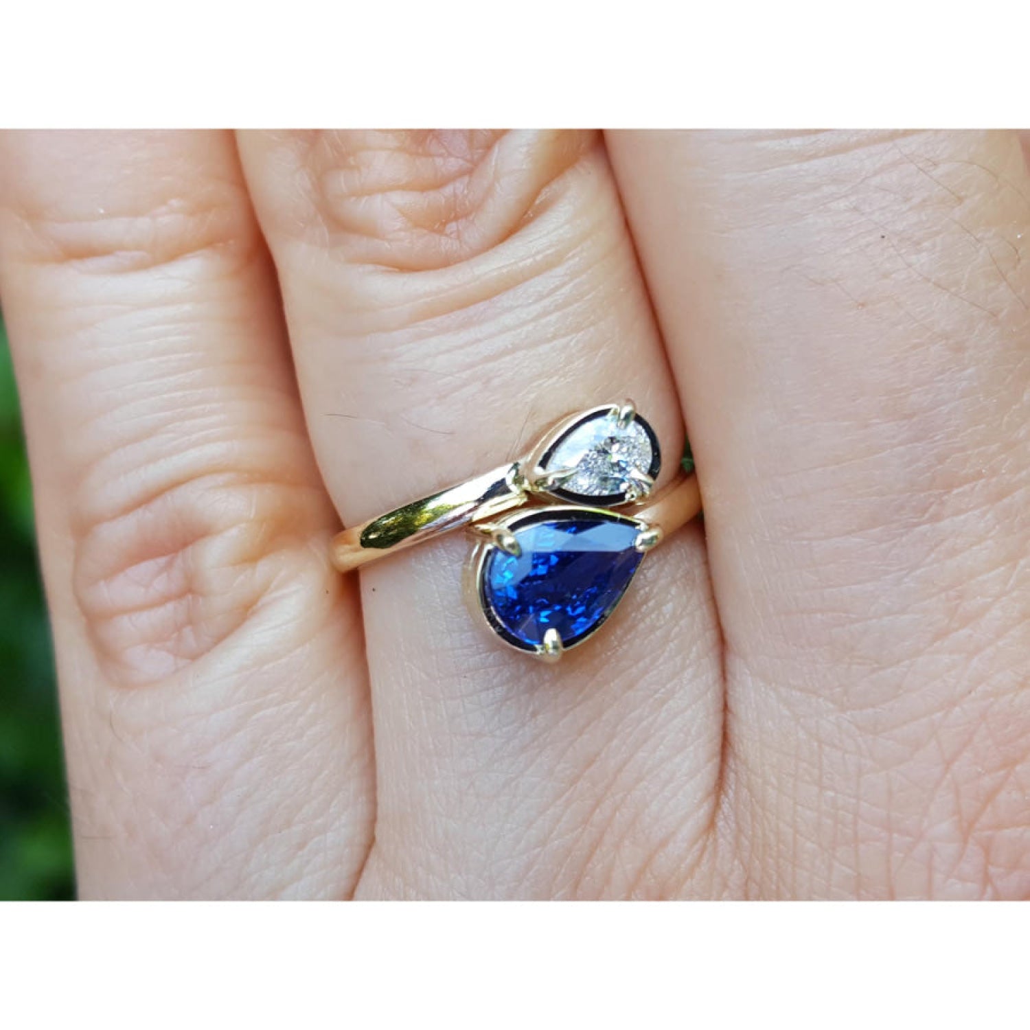 Two-stone "You and Me" blue natural sapphire bypass ring featuring a sparkling medium-deep blue teardrop diamond on the side, handcrafted in 18k yellow gold.