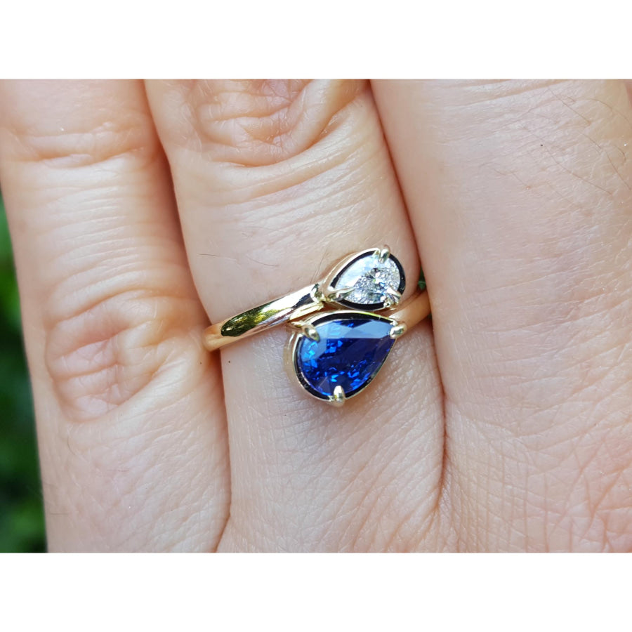 Two-stone "You and Me" blue natural sapphire bypass ring featuring a sparkling medium-deep blue teardrop diamond on the side, handcrafted in 18k yellow gold.
