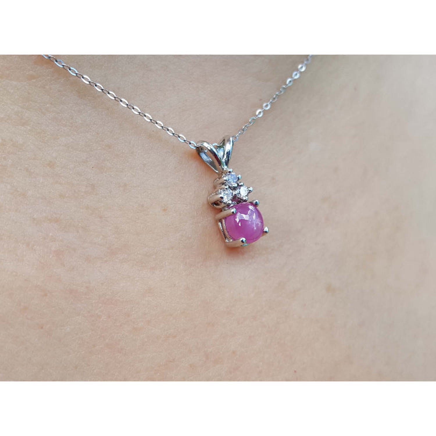 Pink natural sapphire cabochon and diamond necklace on a person's neck.