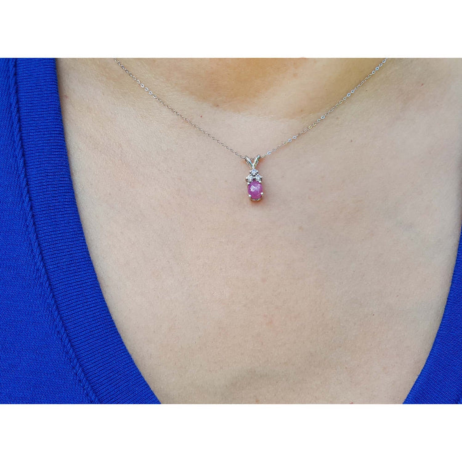 Necklace with a pink sapphire pendant on a person wearing a blue top.