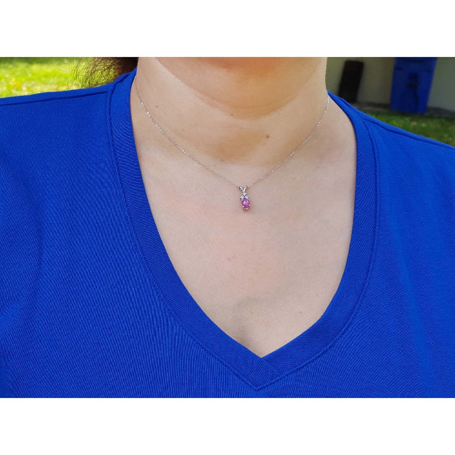 Person wearing a blue shirt with a necklace featuring a small pink sapphire pendant.