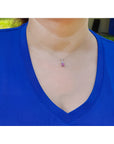Person wearing a blue shirt with a necklace featuring a small pink sapphire pendant.