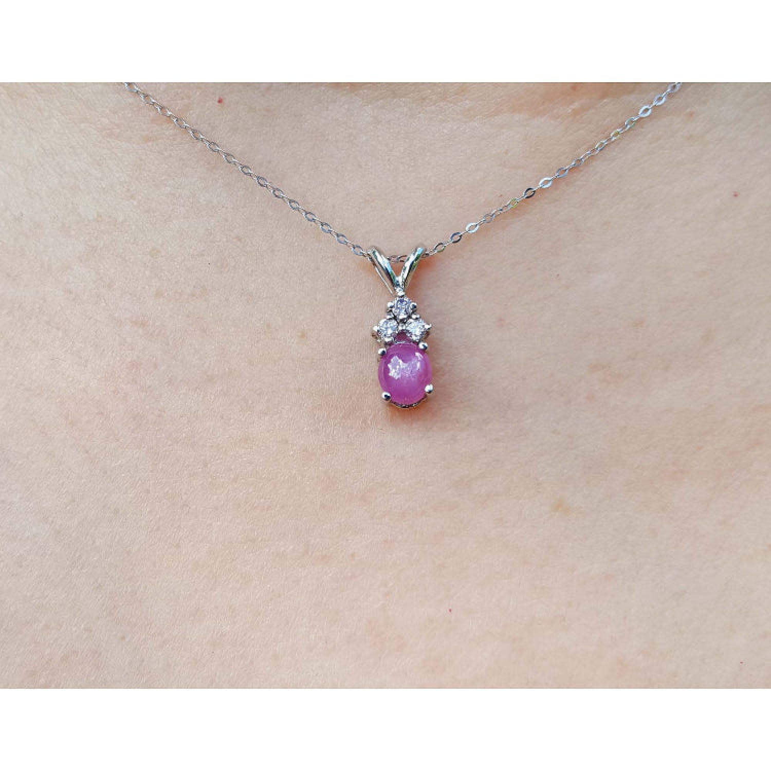 Pink cabochon sapphire pendant on a white gold chain against a skin background.