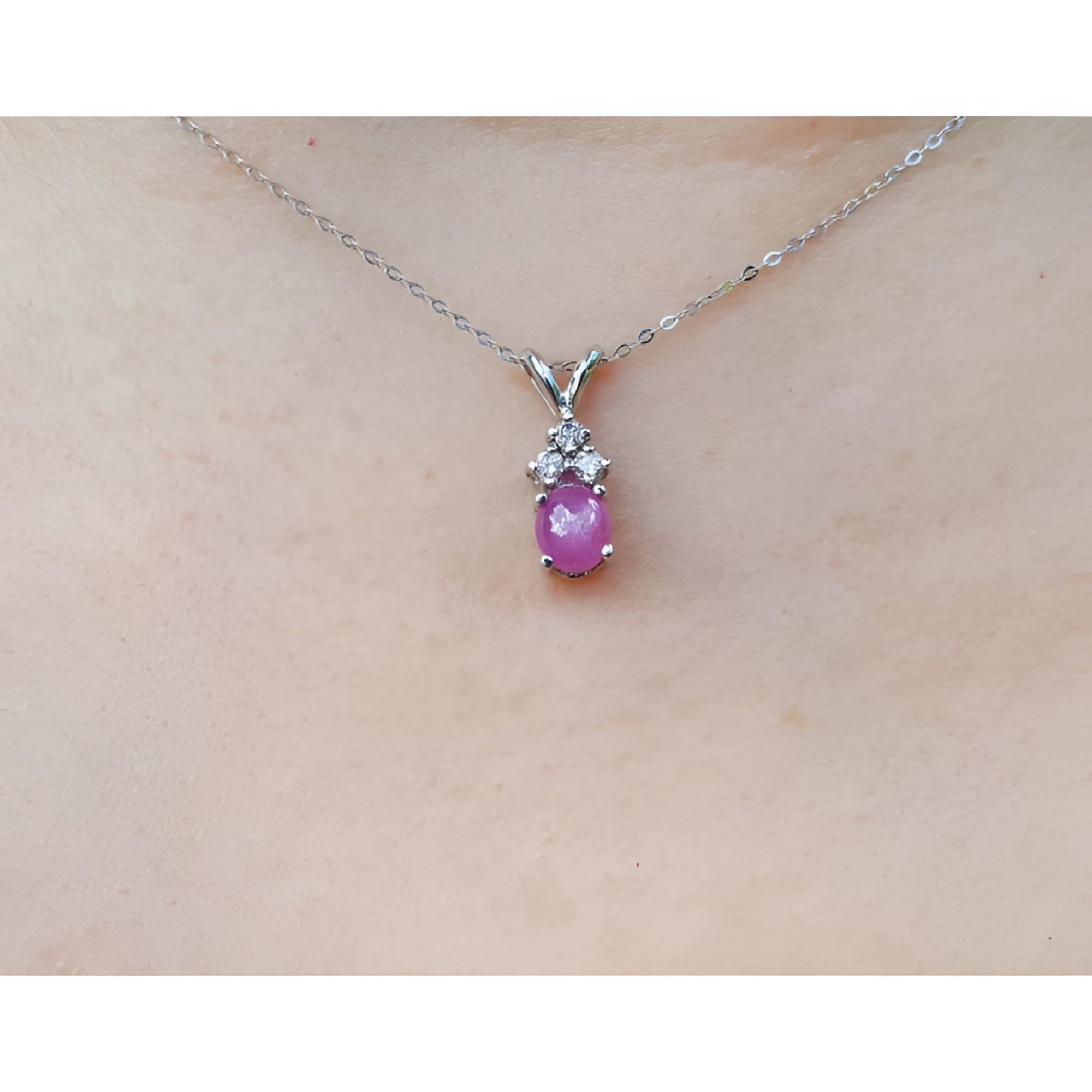 Pink cabochon sapphire pendant on a white gold chain against a skin background.