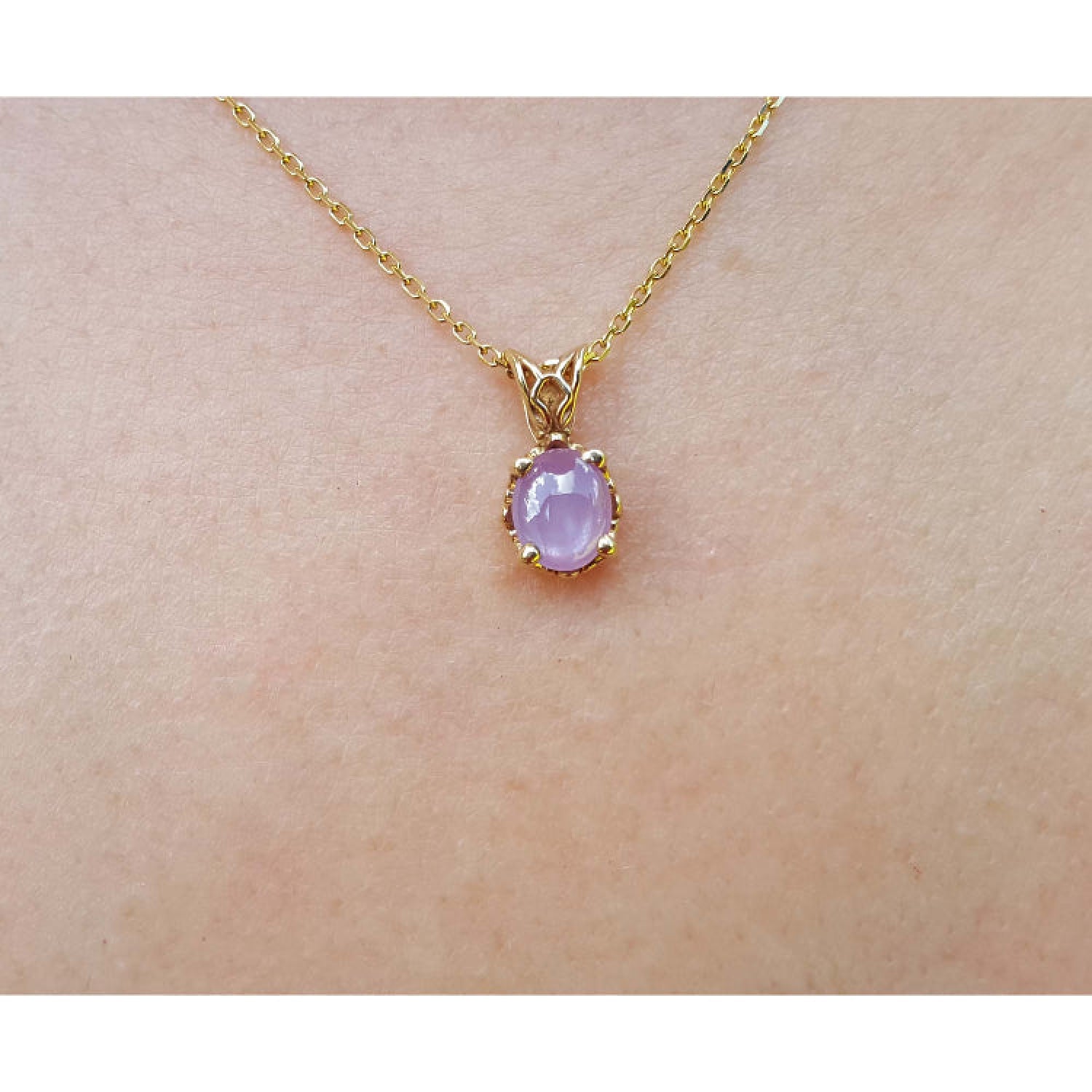 Gold necklace with a pink sapphire solitaire pendant on a skin background.
