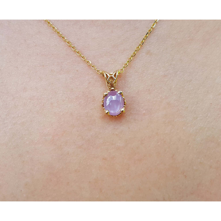 Gold necklace with a pink sapphire solitaire pendant on a skin background.