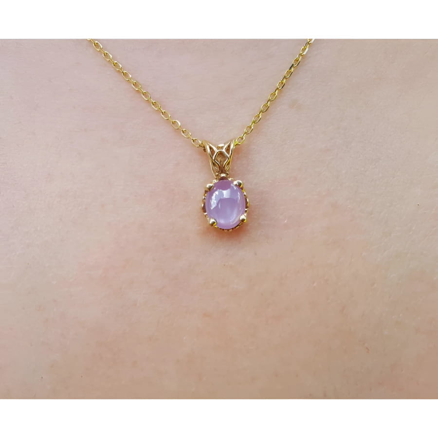 Gold necklace with a pink sapphire solitaire pendant on a skin background.