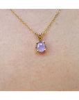 Gold necklace with a pink sapphire solitaire pendant on a skin background.