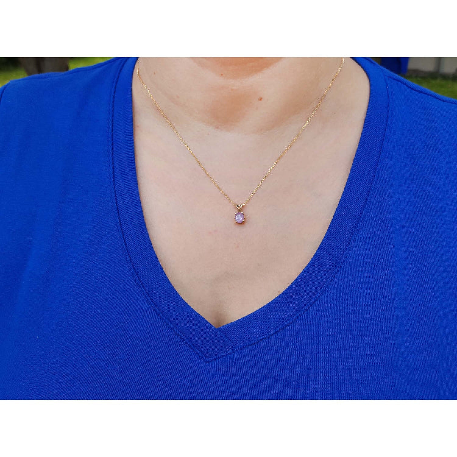 Person wearing a blue shirt with a gold necklace featuring a purple sapphire solitaire pendant.