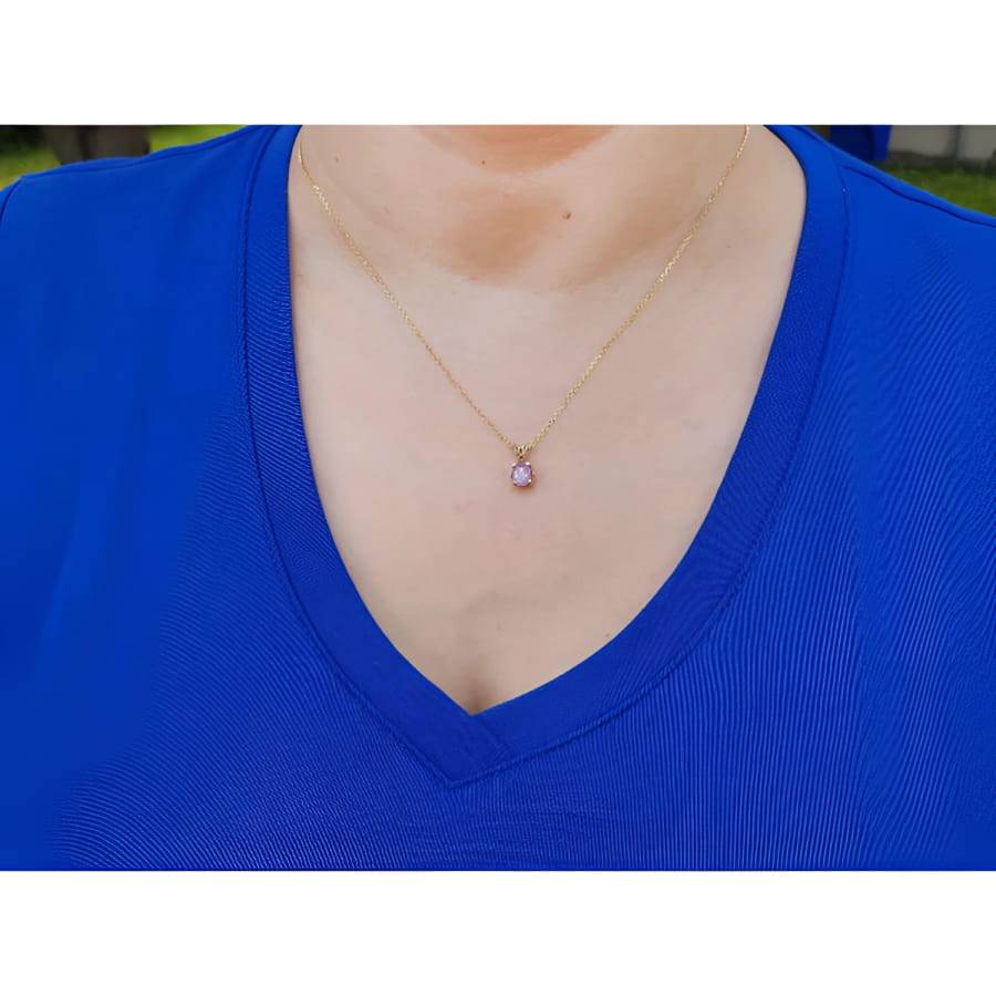 Person wearing a blue shirt with a gold necklace featuring a purple sapphire solitaire pendant.