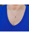 Person wearing a blue shirt with a gold necklace featuring a purple sapphire solitaire pendant.
