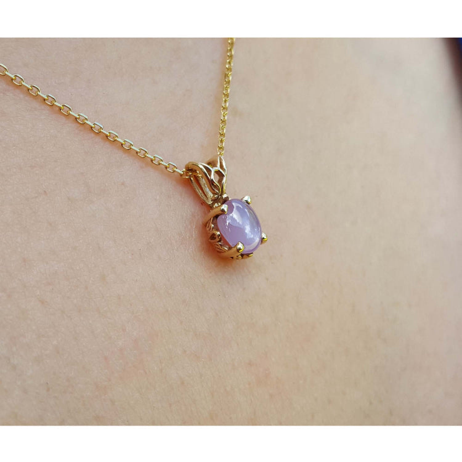 Gold necklace with a pink sapphire pendant on a person's neck.
