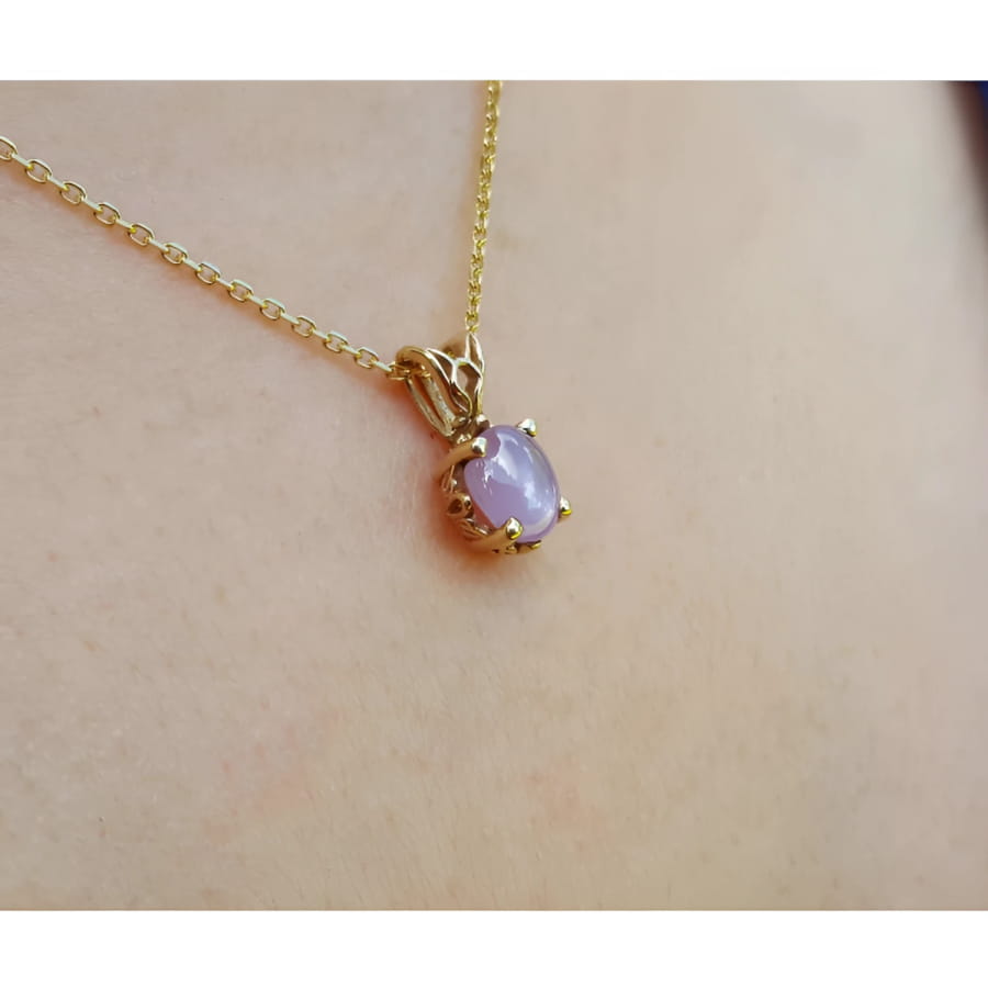 Gold necklace with a pink sapphire pendant on a person's neck.