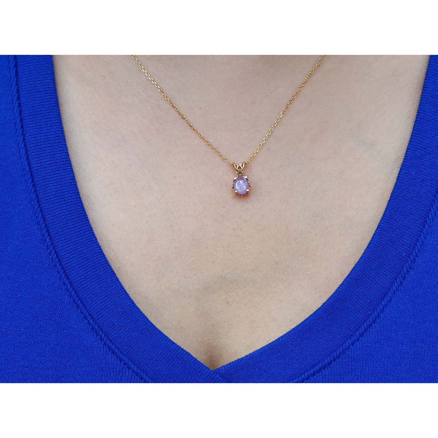 Gold necklace with a purple cabochon solitaire sapphire pendant on a person wearing a blue top.