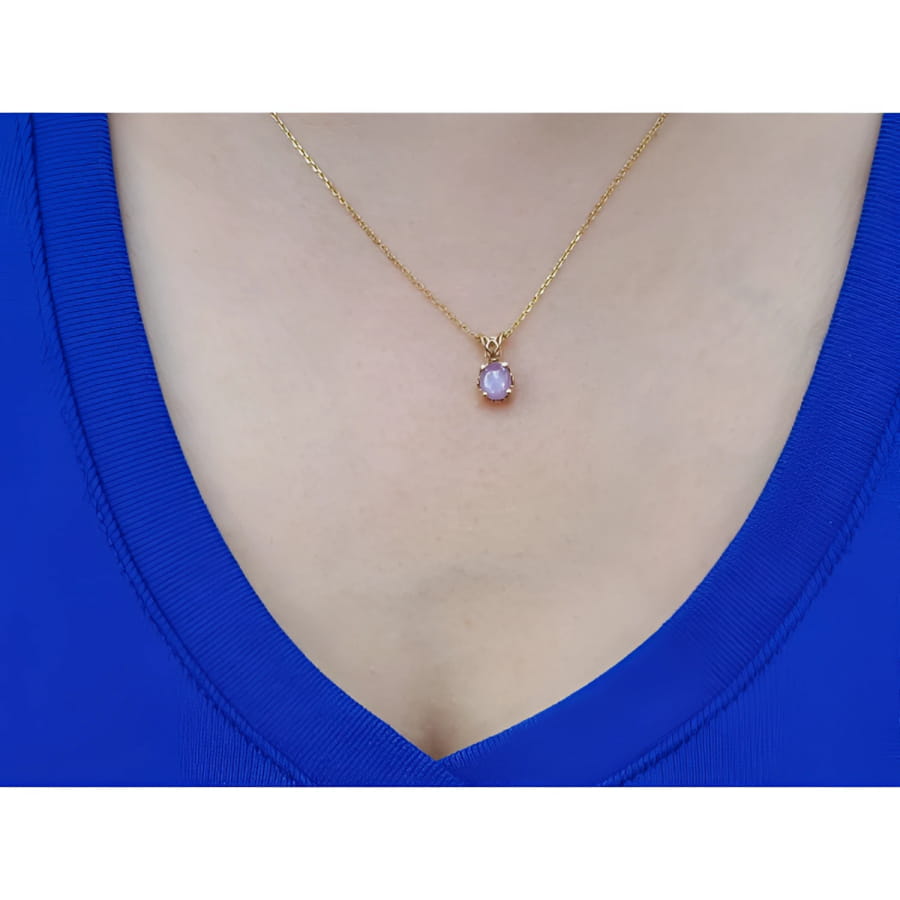 Gold necklace with a purple cabochon solitaire sapphire pendant on a person wearing a blue top.