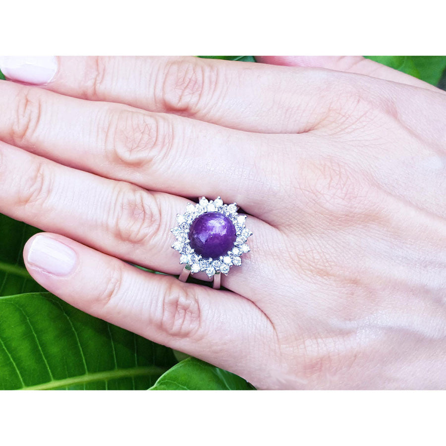 Red purple cabochon star ruby women's ring on a hand against a green leaf background