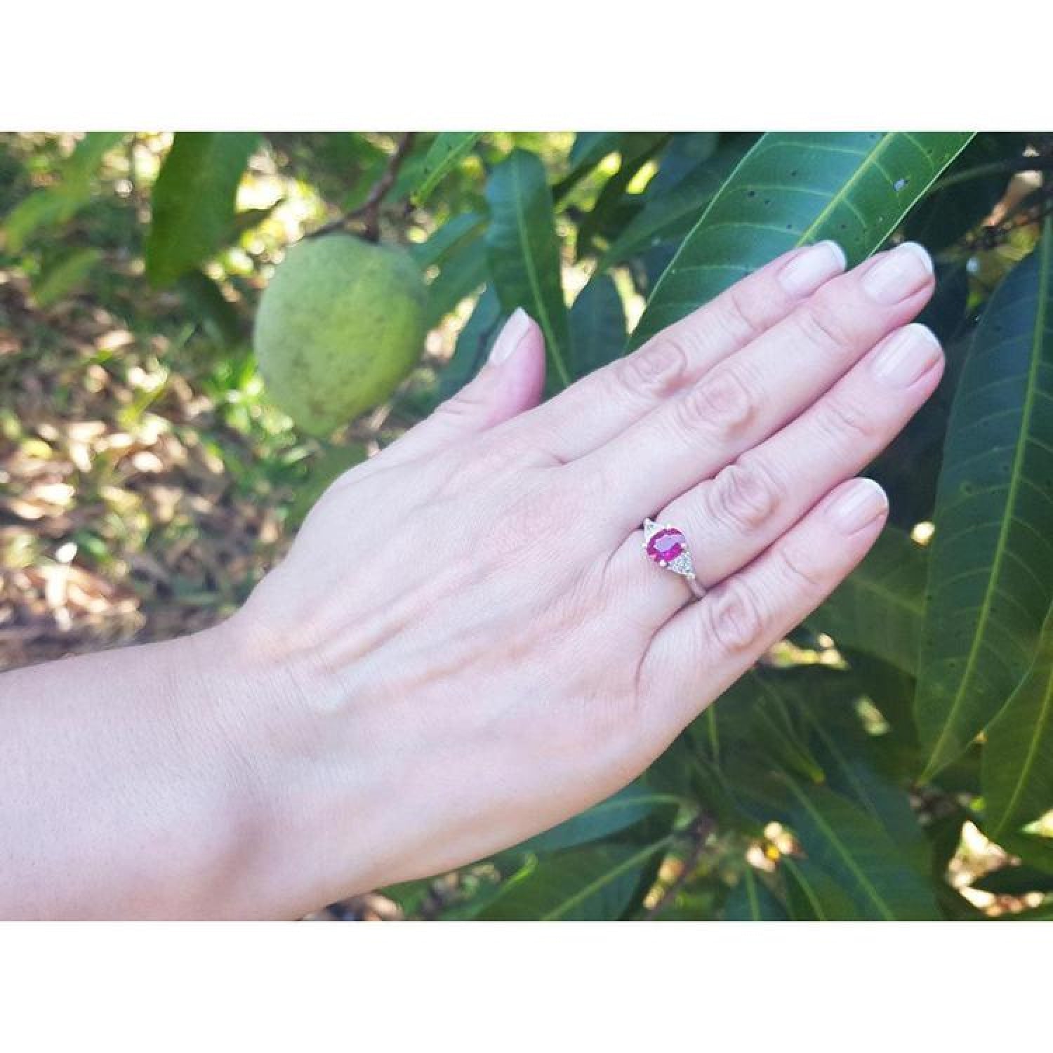 Women's 14k white gold ring with a deep red ruby and trillion side diamonds on a hand.