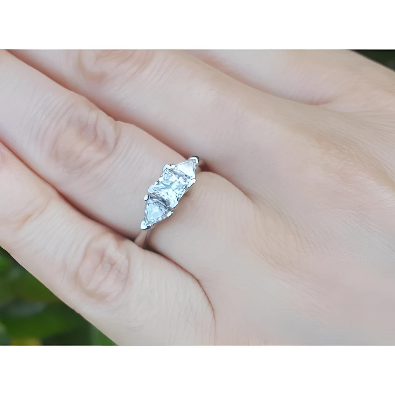 14K white gold ring with a princess cut diamond flanked by two trillion side diamonds on a hand.