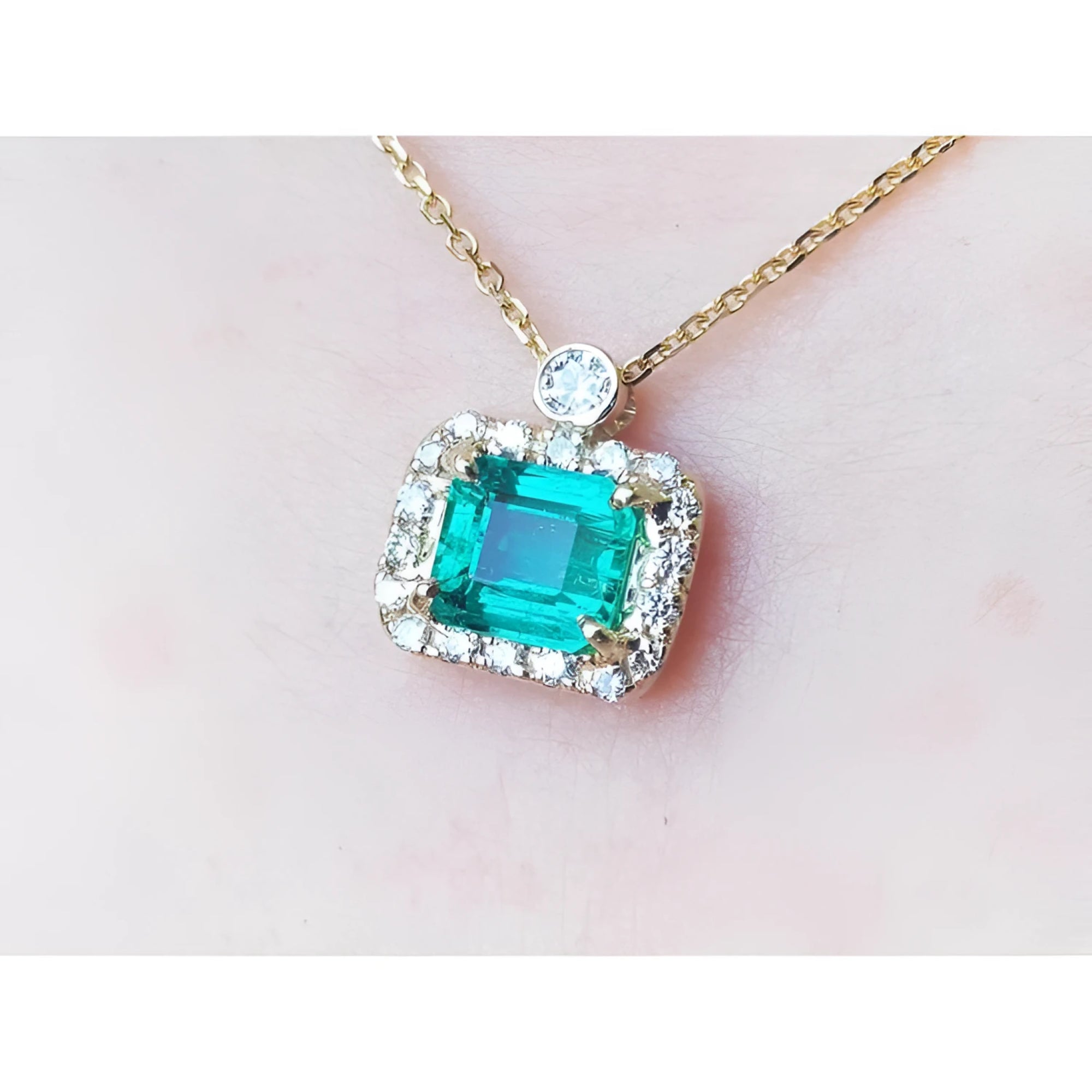 1.31 ct emerald-cut Muzo Colombian emerald necklace with diamond halo on 14K yellow gold chain.