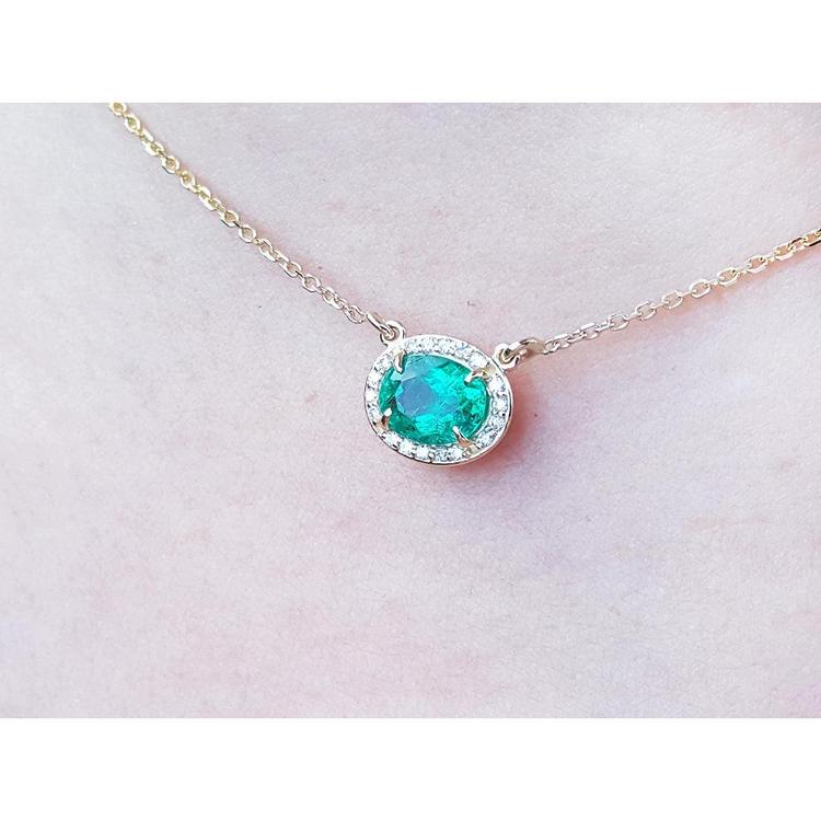 Oval Muzo emerald necklace with diamond halo on a delicate 14K yellow gold chain.