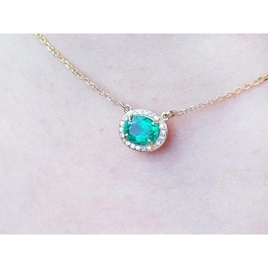 Oval Muzo emerald necklace with diamond halo on a delicate 14K yellow gold chain.