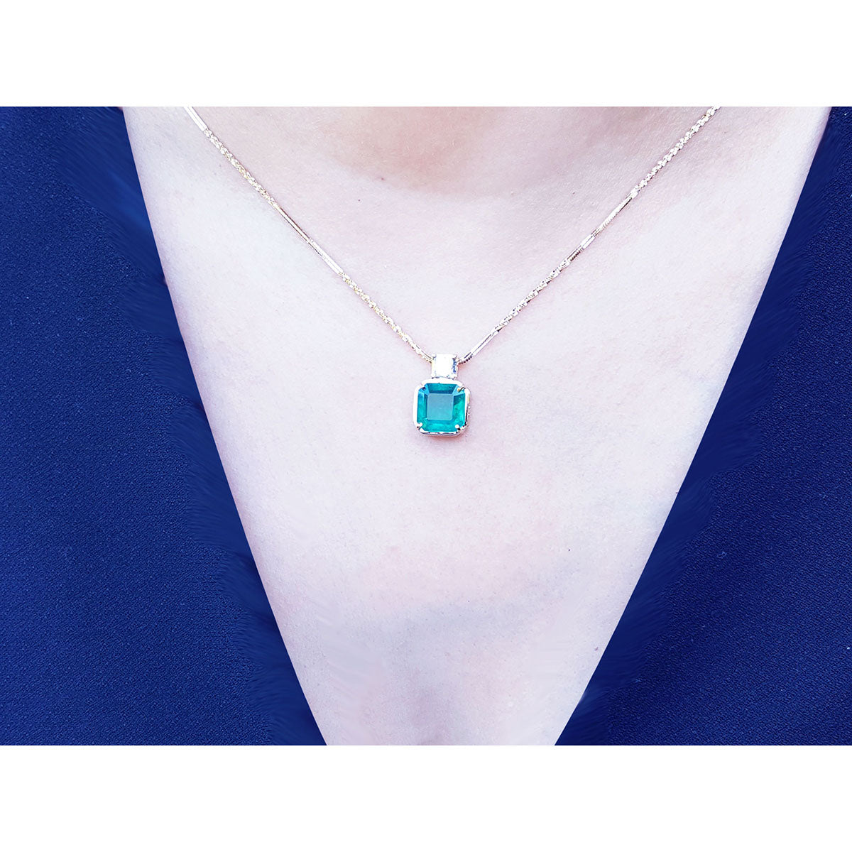 Necklace with an Asscher cut natural Colombian emerald pendant on a person wearing a blue top.