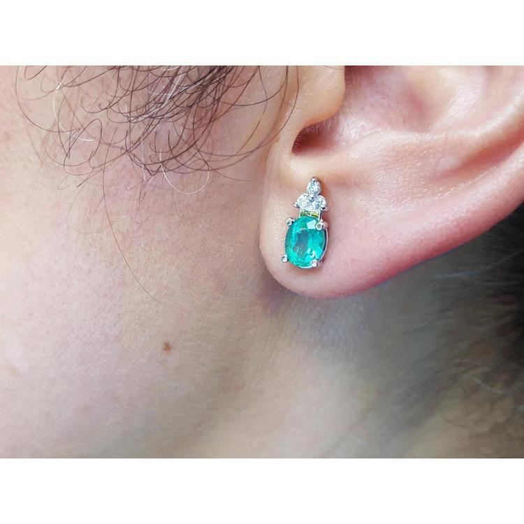 Close-up of an ear wearing a diamond and emerald earring.