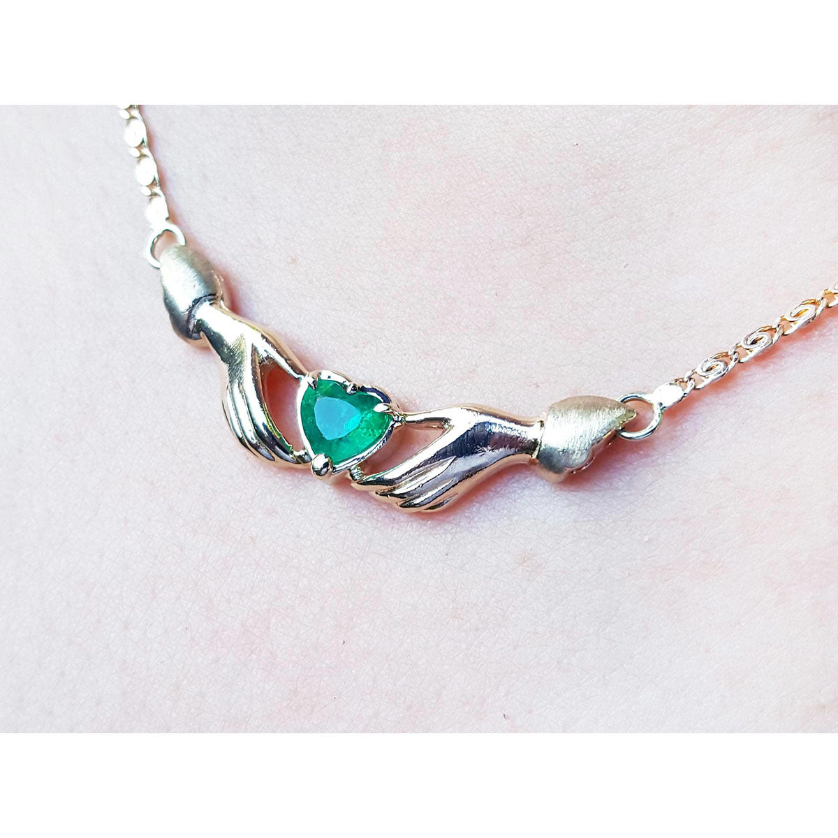 A close display of a hearth cut necklace Claddagh natural emerald Muzo mines crafted in 14k yellow gold
