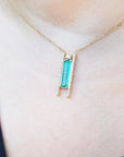 Lady'd gold necklace with a green gemstone emerald pendant on a person wearing a black top.