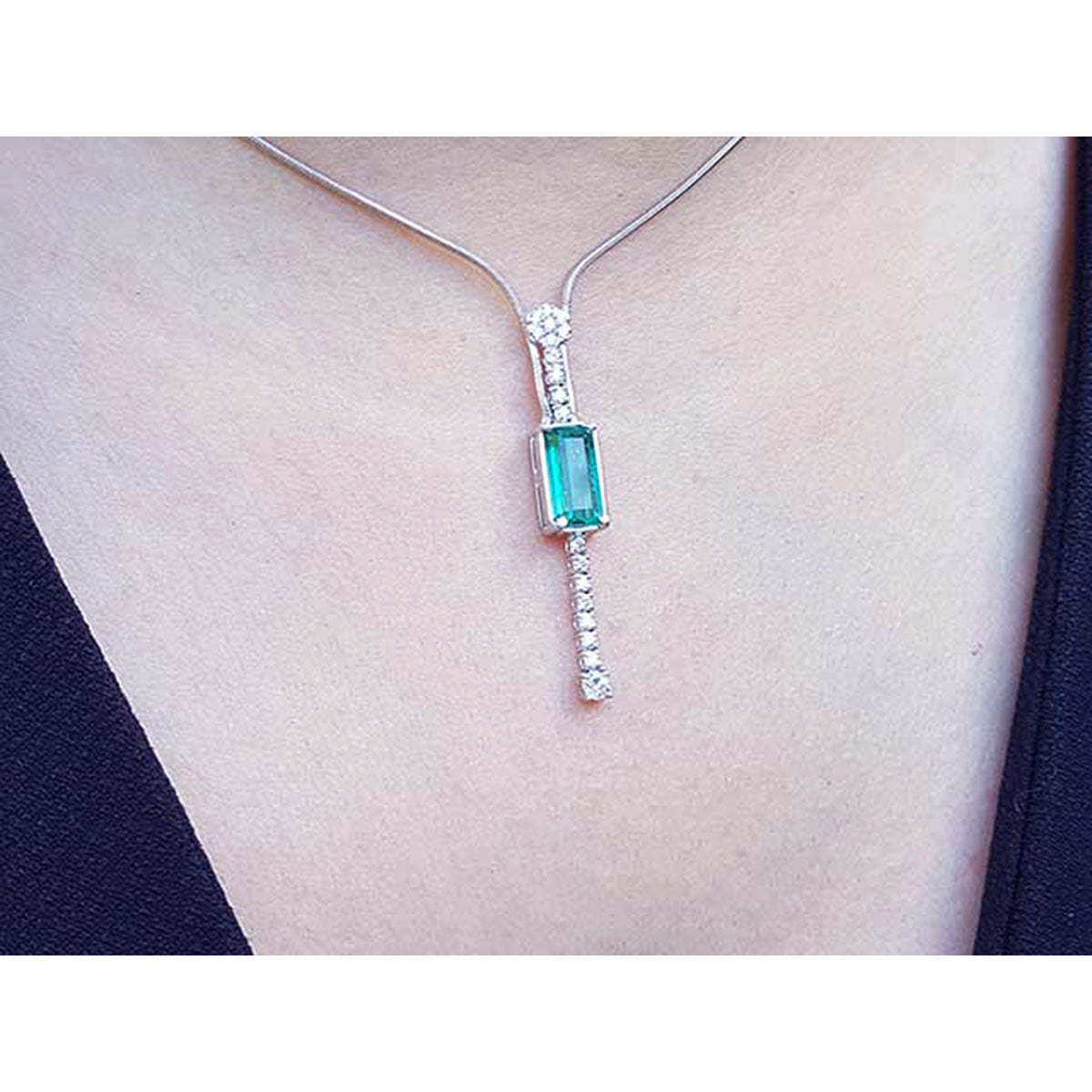 Close view of a white gold necklace with an emerald gemstone pendant on a person&#39;s neck
