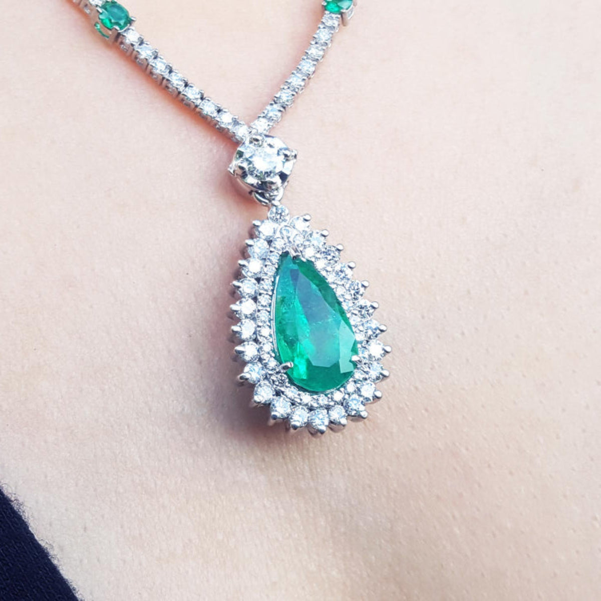 closer view of an emerald necklace with a green teardrop pendant on a women&#39;s neck